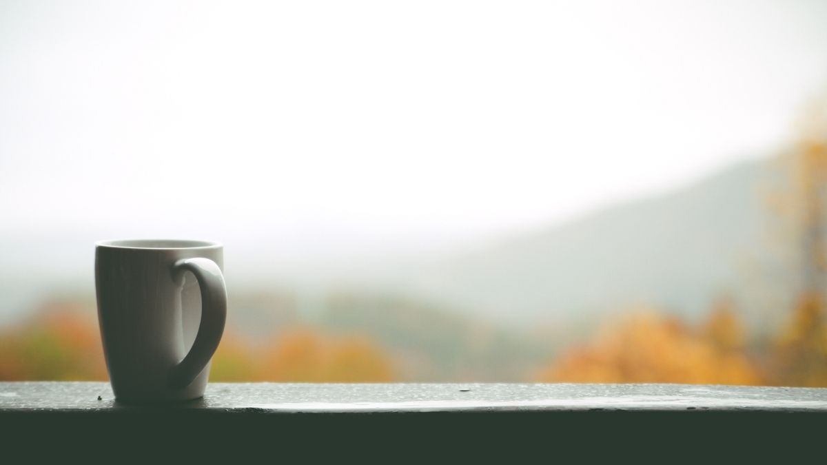 coffee mug on table before misty mountains