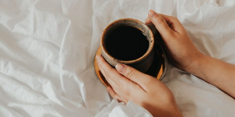 person holding a cup of morning coffee on their bed