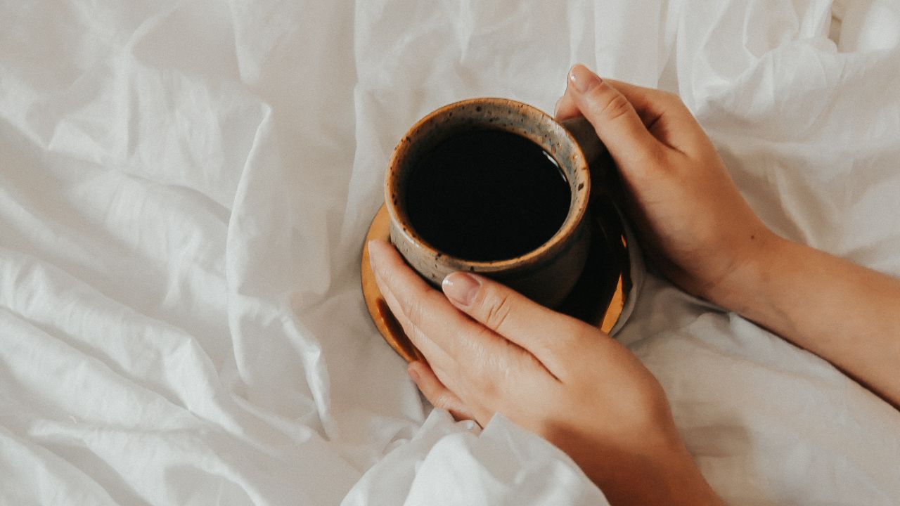 person holding a cup of morning coffee on their bed