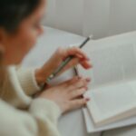 young woman reading a book and writing in her journal