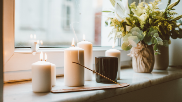 incense and candles with a plant on a shelf by a window